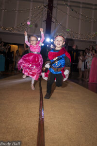 A little boy and girl in fairy tale costumes running down the gold carpet at the Miracle Party.