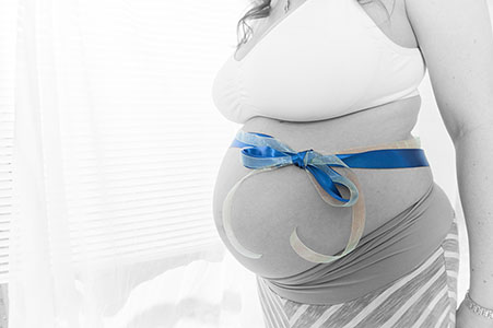 black and white image of pregnant belly with a blue ribbon tied around it