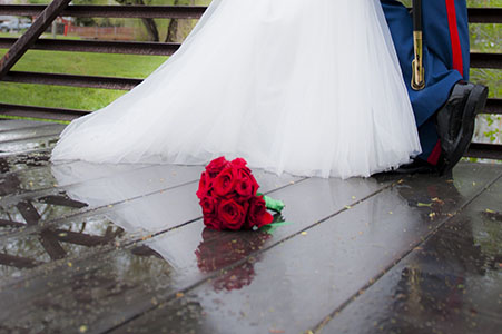 Bouquet of red roses laying on wet bridge in front of bride's gown and US Marine's dress blue.