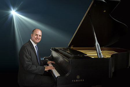 Adult male in suit playing baby grand piano in studio