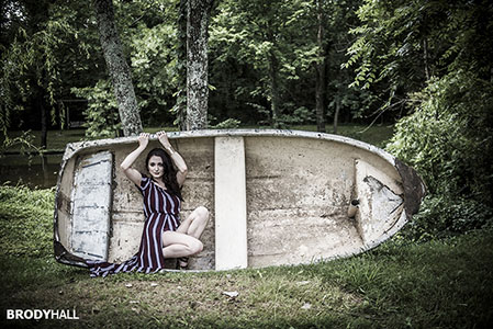 Adult female in stripped dress kneeling in upturned boat at Sinking Creek Farms, Murfreesboro, TN.