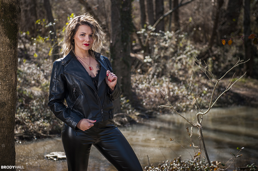Brittany in leather jacket and pants in woods.