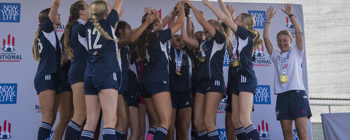 Female soccer team on stage holding their newly won national trophy.