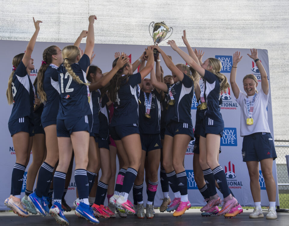 Female soccer team on stage holding their newly won national trophy.