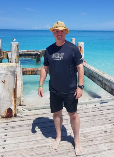 Turks & Caicos Brody standing on the docks in the Turks and Caicos islands, turquoise water in the background.