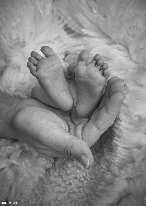 Black and white image of Baby's feet being held by mother's hands.