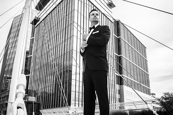 Black and white image of man in tuxedo standing in front of large glass building