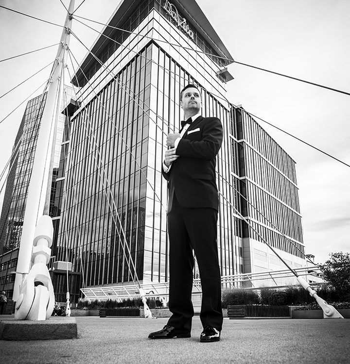 Black and white image of man in tuxedo standing in front of large glass building