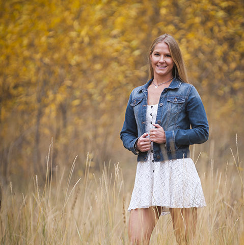 Young lady in jean jacket and white skirt standing amid field of tall grass