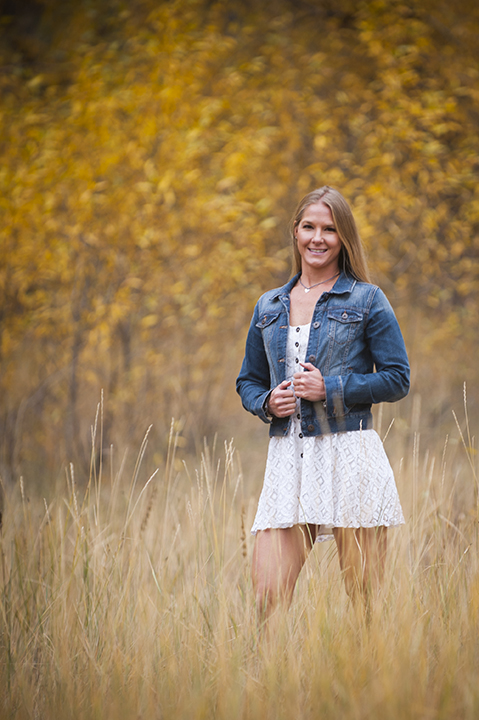 Young lady in jean jacket and white skirt standing amid field of tall grass