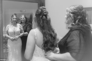 Bride and mother looking at each other in the mirror as the mom buttons up the wedding dress.