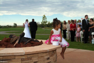 The flower girl decided to not go down the aisle, so she sat down on a small wall and watched the wedding.