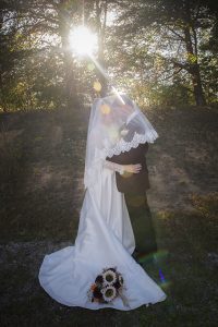 Bride and groom embracing beneath her flowing wedding veil as sunlight streams through the trees at a country wedding in Middle Tennessee.