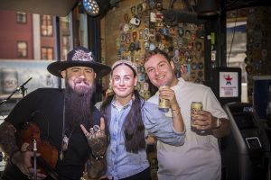 Yitzy and Leah posing with a fiddle player inside a Nashville honky-tonk during their downtown couples photo shoot.